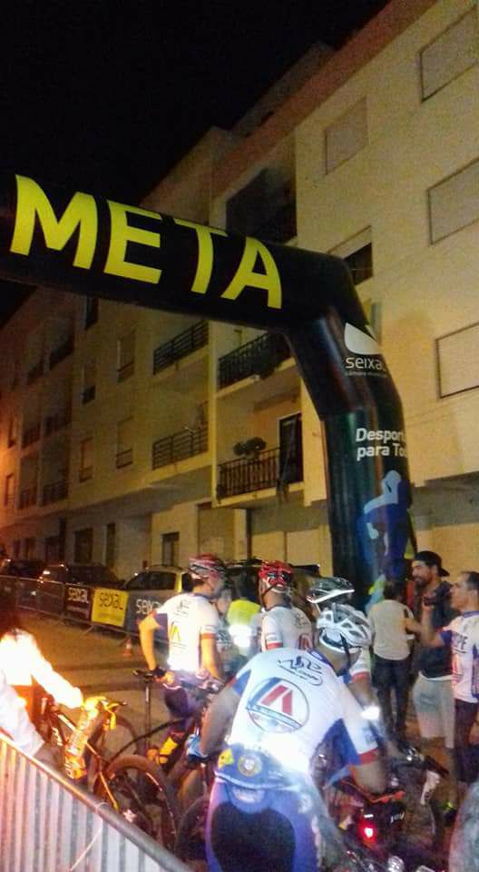 Arco de meta iluminado com ciclistas durante prova noturna